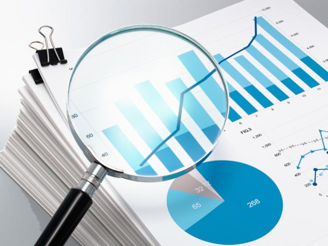 A magnifying glass placed over printed charts showing bar and line graphs, alongside a pie chart, representing data analysis.
